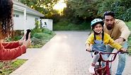 Mother, father and kid on bike learning in driveway with phone to record video, photograph or family support. Excited parents teaching happy girl on bicycle with mobile for memory, fun games and care