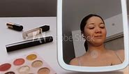 Korean female person applying pink blush on cheeks and smiling in the mirror. Asian woman making up nude visage. Natural make-up. Morning routine. Film grain pixel texture. Soft focus. Blur.