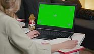 Chromakey Mockup. Woman writing and using laptop with blank green screen.