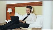 Happy businessman in headphones working at laptop computer and listening music smiling while lying