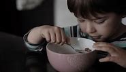 Little Hungry Boy Eating Breakfast Corn Cereal From Plate Sitting Home at Table in Kitchen. Child Eat Cornflakes with Milk. Healthy Nutrition Flakes. Portrait of Kid Eating Eating Muesli for Breakfast