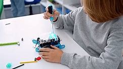 Robotics programming class. Child construct Mbot screwdriver and code Robot. STEM education using constructor blocks and laptop tablet, remote control joystick. Technology educational development for