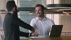 Confident caucasian male financial advisor bank worker broker explaining deal benefits, showing presentation on computer to focused arabic businessman, shaking hands after making agreement in office.