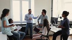 Young male international company department leader talk to smiling multiracial colleagues on brief meeting at workplace share plans with staff. Diverse teammates friends discuss job issues on seminar
