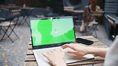 Camera view of woman working at laptop with green screen. Typing something on keyboard while sitting at table in cafe. Working remotely on her technology device. Chroma key. Concept of computer.