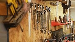 Copper metal wire, a set of bits and screwdrivers, wrenches, hexagons and other tools hang on a wooden wall in a repair shop. Move focus from foreground to background