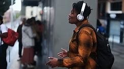 Young african woman listening music with wireless headphones while waiting at tram station