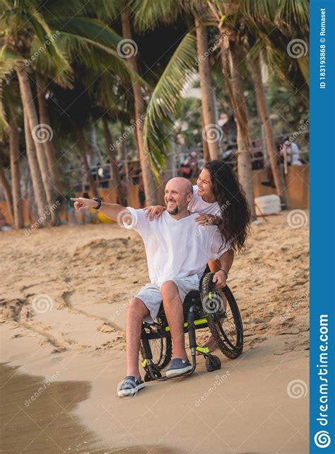Disabled Man In A Wheelchair With His Wife On The Beach