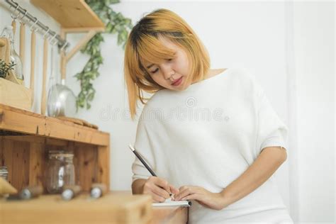 Asian Woman Write Shopping Lists In Notepad By Pen On Her Kitchen