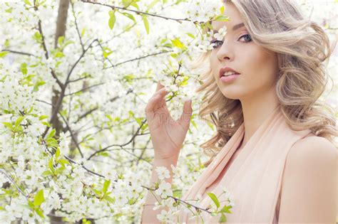 beautiful elegant sweet blue eyed blonde girl in the garden near the cherry blossoms on a sunny