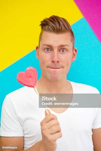 Portrait Of Handsome Blond Man Licking On Heart Shaped Lollipop Stock