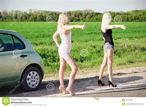Two Blonde Girls Standing Near Their Broken Car And Hitchhiking Stock
