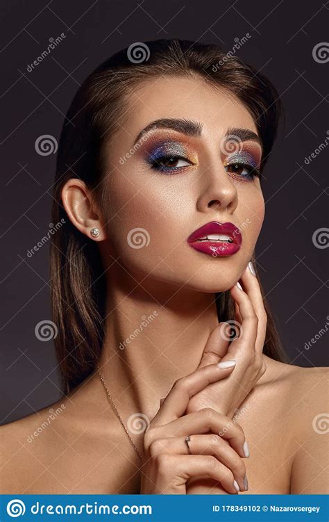naked lady in jewelry is touching her face posing on gray background