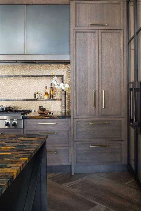 brown oak kitchen cabinets accented  brass pulls   gold  black marble countertop