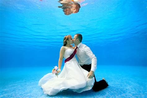 The Bride And Groom In Wedding Dresses Embrace And Kiss Underwater At