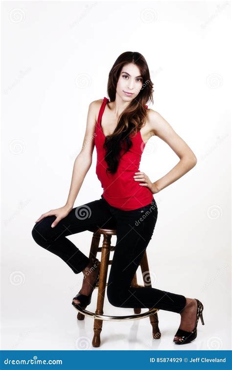 Skinny Latina Woman Sitting On Stool Red Top Blue Jeans Stock Image