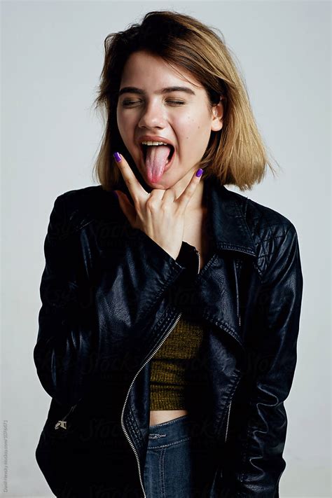 teen girl with sign of horns sticking out tongue by stocksy