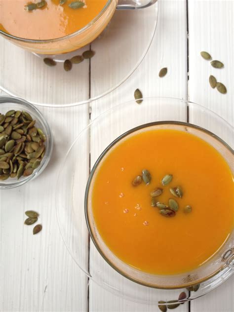 bowls filled  carrot soup  topped  pumpkin seeds   white wooden table