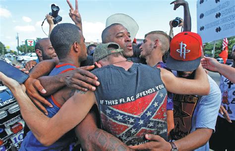 people including a man wearing a confederate flag hug after taking part in a prayer circle after