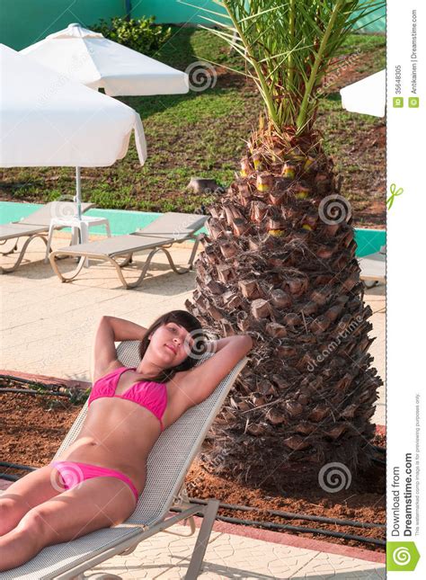 woman in bikini laying on lounge under palm tree stock