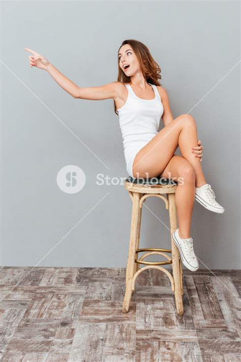 Amazed Charming Woman Sitting On The Chair And Pointing Away Isolated