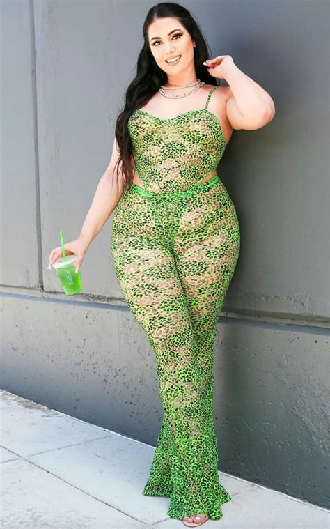 A Woman In Green And Gold Lace Jumpsuits Leaning Against A Wall With