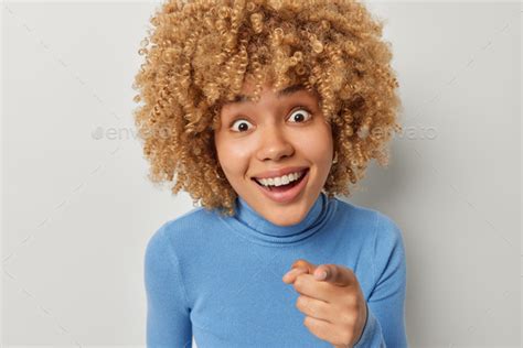 surprised curly haired woman stares impressed indicates index finger
