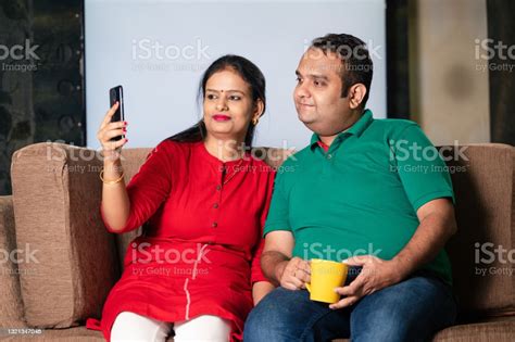 Young Indian Couple Sitting Together On Sofa And Taking Selfie With