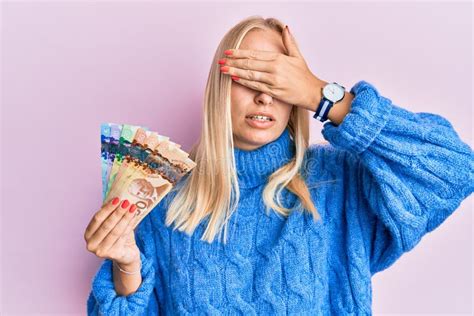 young blonde girl holding canadian dollars covering eyes  hand
