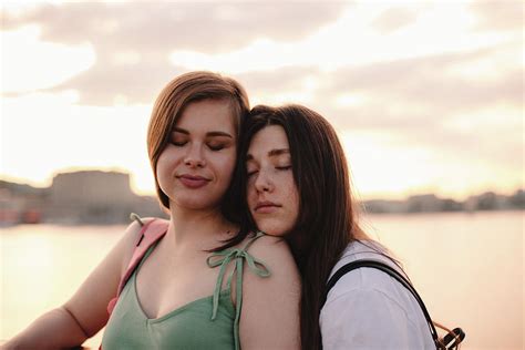 Portrait Of Happy Lesbian Couple Standing On Bridge At Sunset