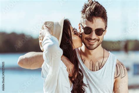 happy interracial couple in sunglasses hugging while girl kissing her