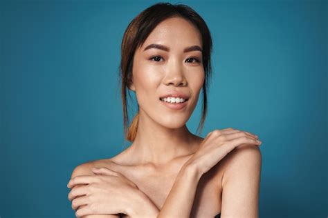 파란색 벽에 알몸으로 포즈를 취한 아름다운 긍정적인 미소 아시아 여성의 사진 프리미엄 사진
