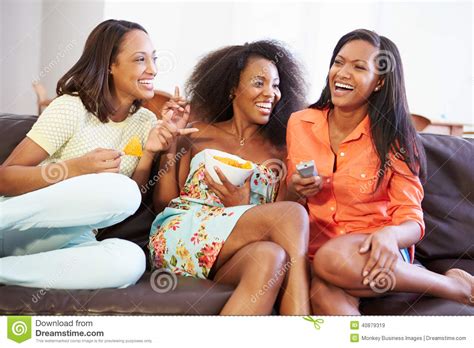 group of women sitting on sofa watching tv together stock