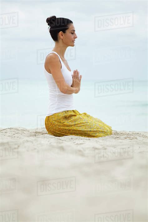 mature woman kneeling in prayer position on beach side view stock