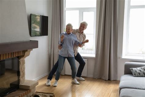 Happy Energetic Older Age Couple Dancing At Modern Living Room Stock