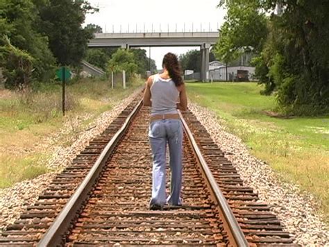 a beautiful latina brunette walks away from the camera down a lonely stretch of railroad track
