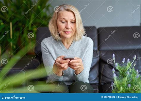 Beautiful Mature Blond Woman Talking On Mobile Phone At Sofa Stock