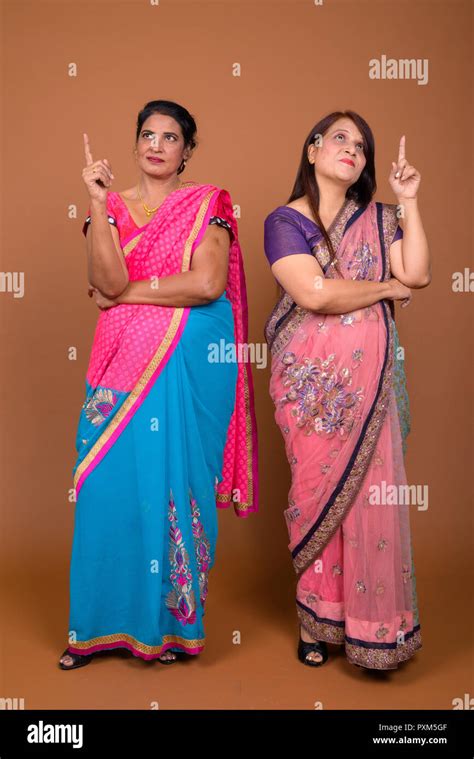 two happy mature indian women wearing traditional clothes and pointing