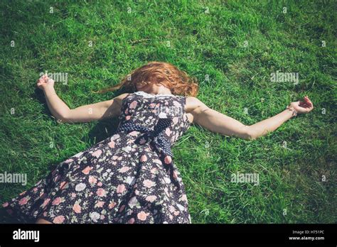 A Young Woman Wearing A Dress Is Lying In The Green Grass On A Sunny