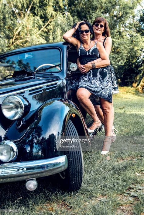 Smiling Mature Lesbian Couple By Their Vintage Gangster Car High Res