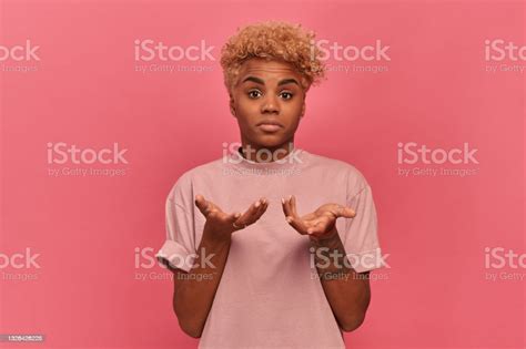 Confused Darkskinned Woman Spreading Her Arms And Shrugging On A Pink