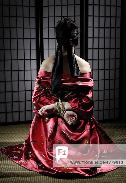 asian woman in red kimono with blindfolded eyes and her hands tied with bondage rope behind her