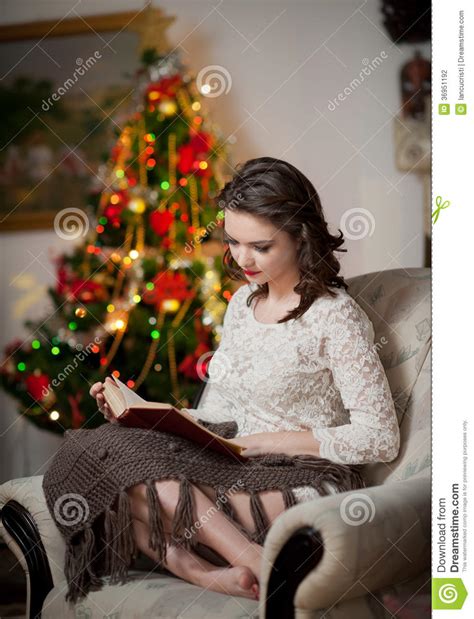 Beautiful Woman With Xmas Tree In Background Reading A Book Sitting On