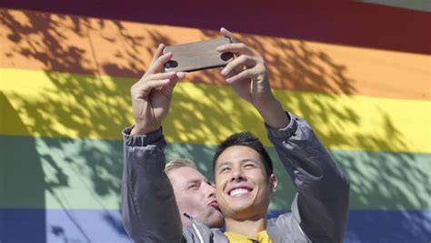 closeup of interracial male couple they kiss gay pride flag in background stock footage video