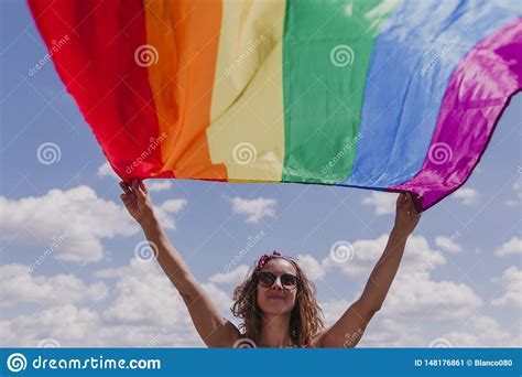 woman holding the gay rainbow flag over blue and cloudy sky outdoors