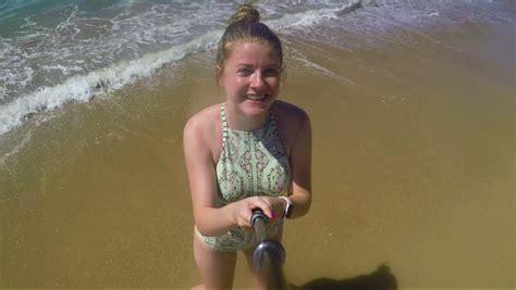 happy teen takes a selfie video on the beach with gopro stick she makes a kissy face and poses