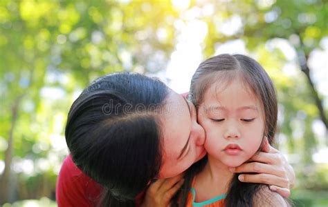 close up asian mother kissing her daughters lying in the summer garden