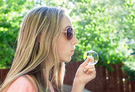 teenage girl with long blonde hair and sunglasses blowing bubbles del