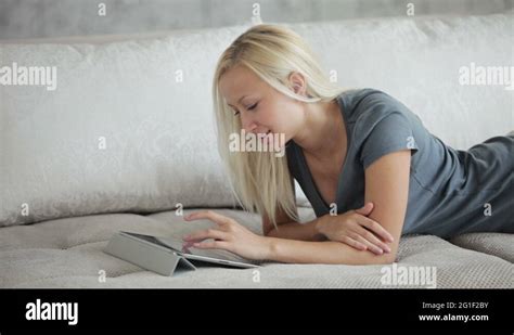 Beautiful Girl Lying On Sofa Using Touchpad And Smiling At Camera Stock