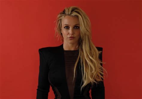 Britney Spears Dressed In Black Shoulder Pad Dress Against Red Wall